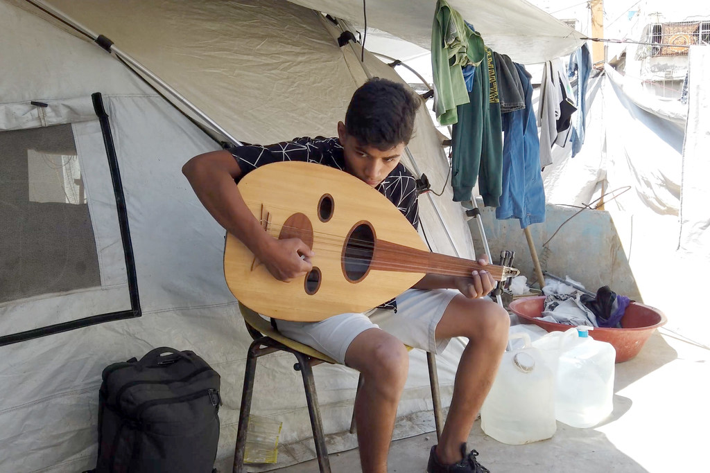 Un garçon joue de la musique à l'intérieur d'une tente à Gaza.